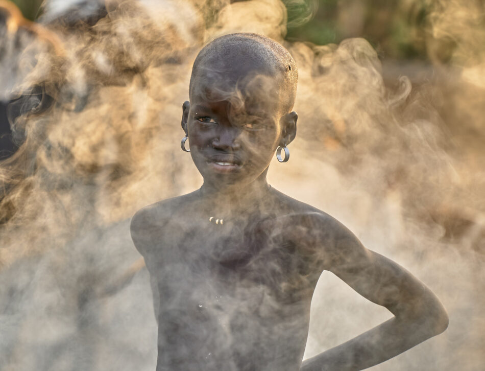 A girl cattlekeeper cares for her cows as smoke from smoldering dung fires swirls about her in Mogok, a rebel-held village in South Sudan. A member of the Nuer tribe, her family and others burn cow dung to keep flies and other insects from bothering their animals.
